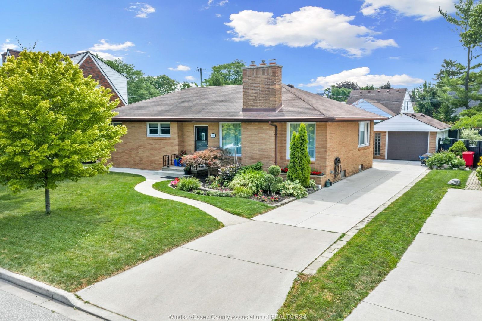 Wide front view showing curved path, driveway, trees and landscaped yard