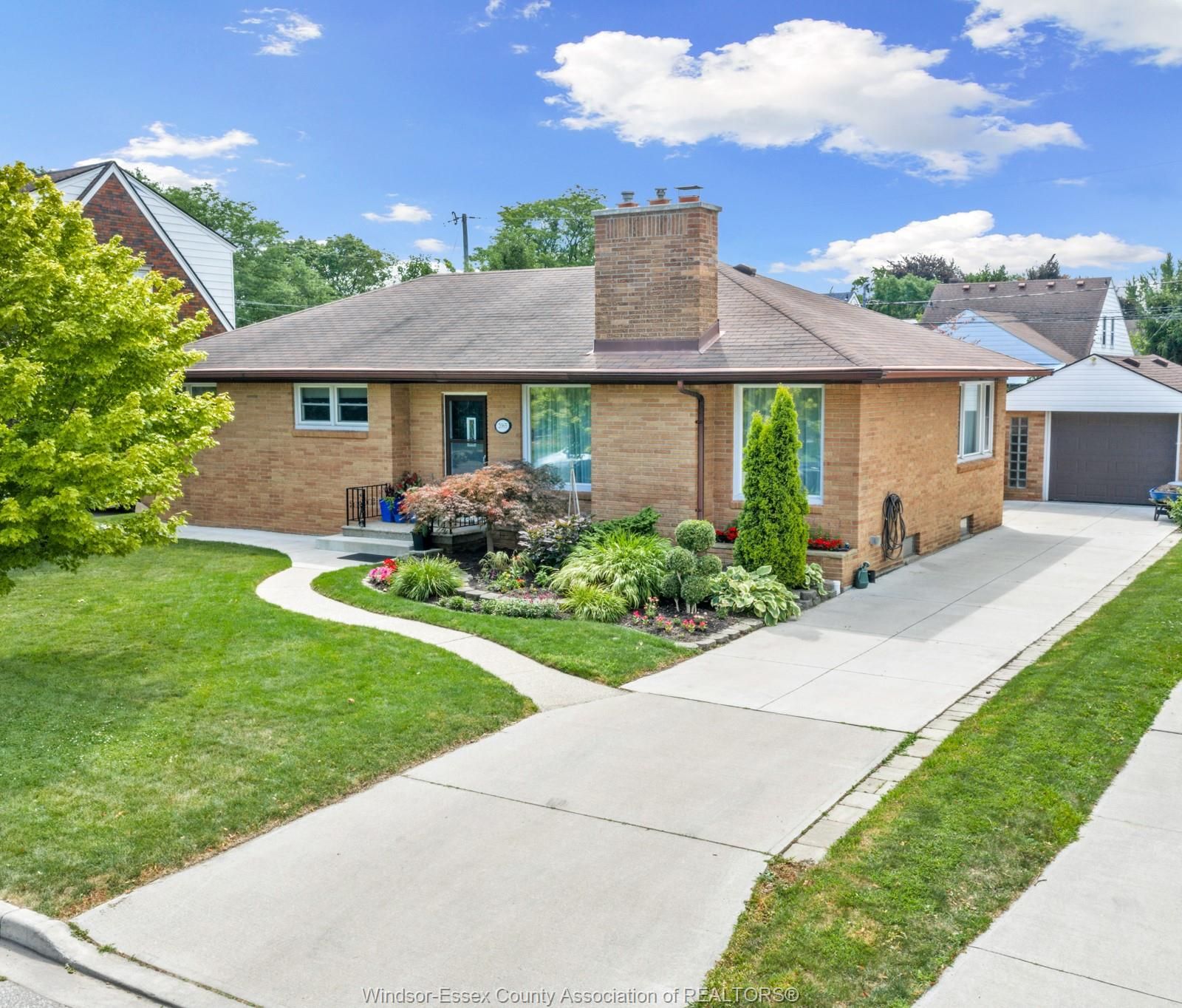Angled front view of the brick ranch with chimney, landscaped lawn and concrete driveway