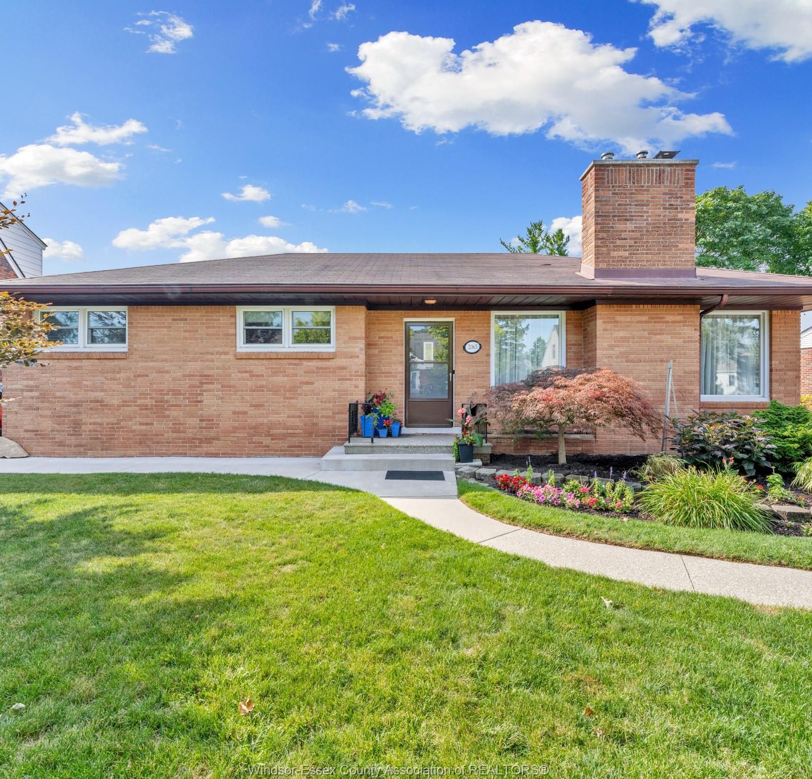 Front elevation of the brick house with front door, windows and flower beds