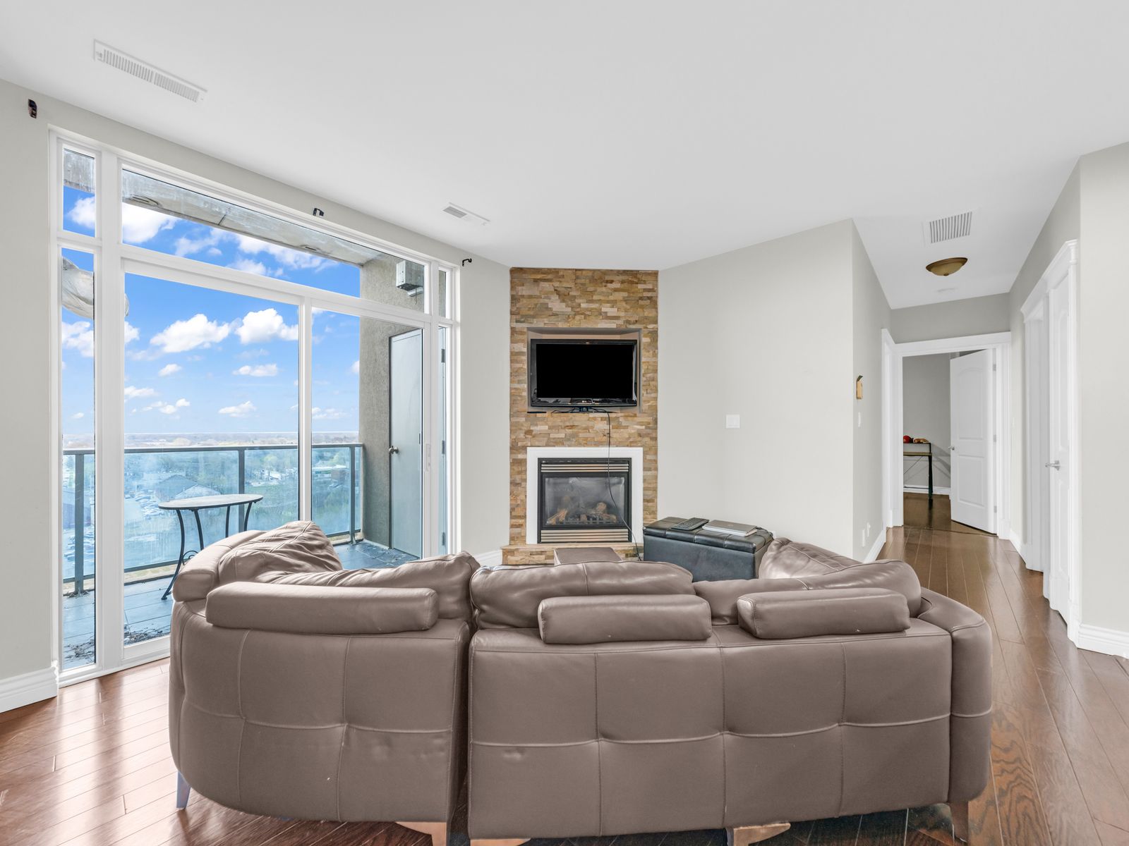 Living room with leather sectional, stone fireplace, and floor-to-ceiling balcony door