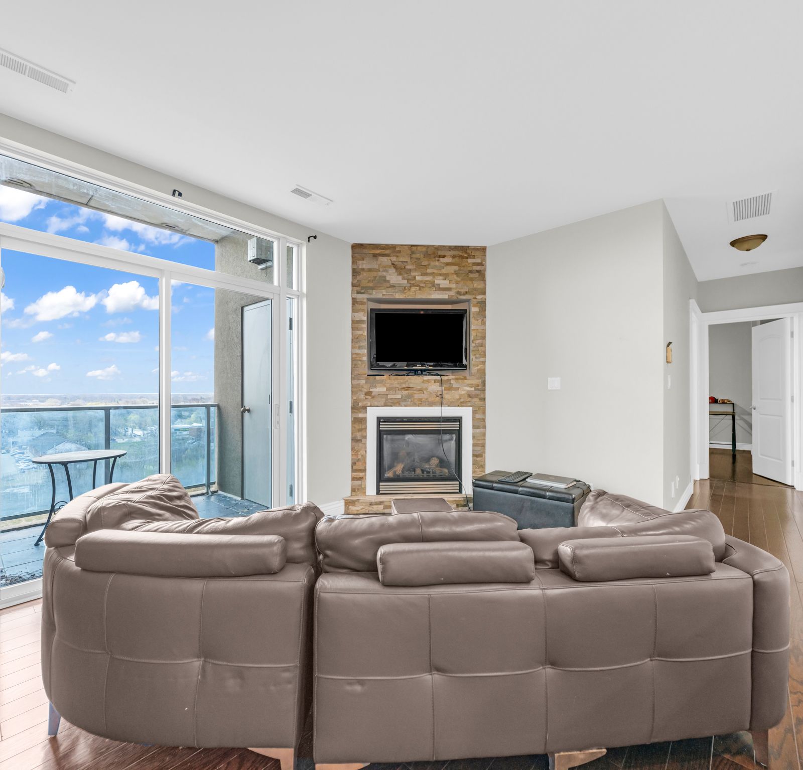 Living room with leather sectional, stone fireplace, and floor-to-ceiling balcony door