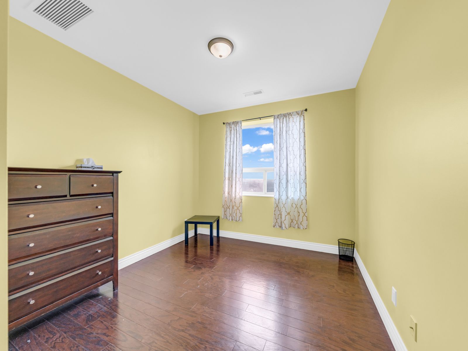 Second bedroom with bright window and wooden dresser