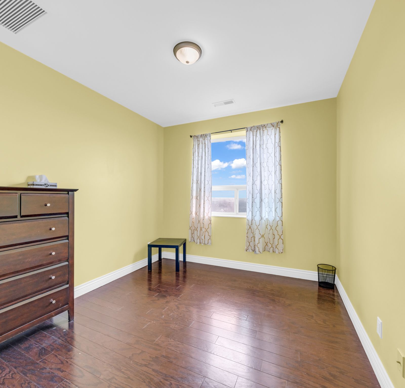 Second bedroom with bright window and wooden dresser