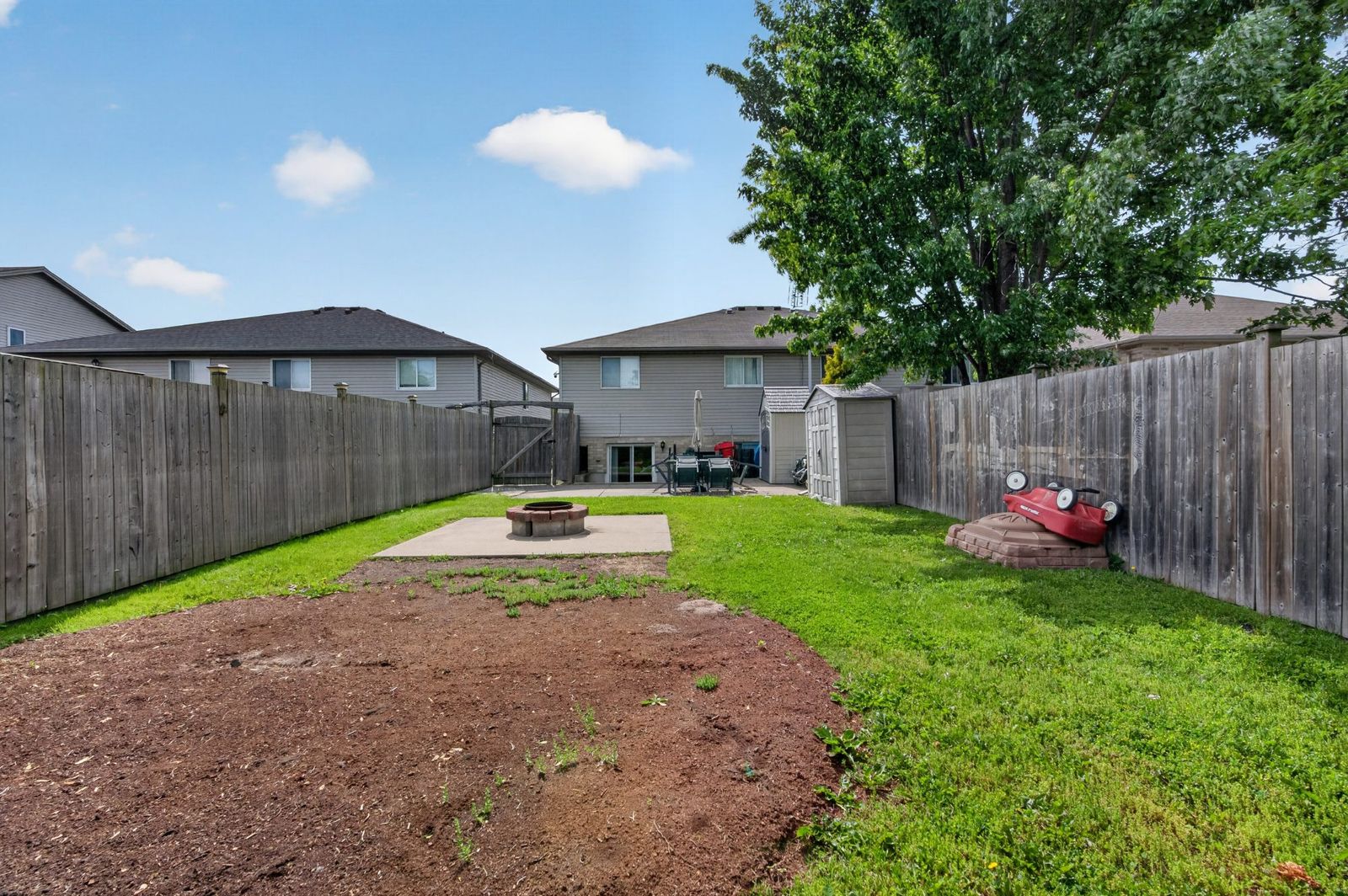 Fenced backyard with fire pit, green lawn, and storage shed