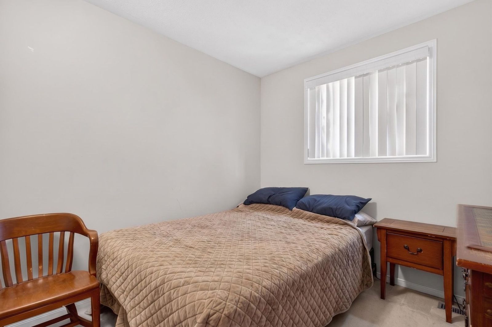 Bedroom with window, wooden furniture, and beige quilt