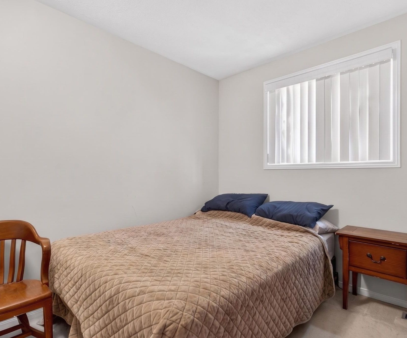 Bedroom with window, wooden furniture, and beige quilt