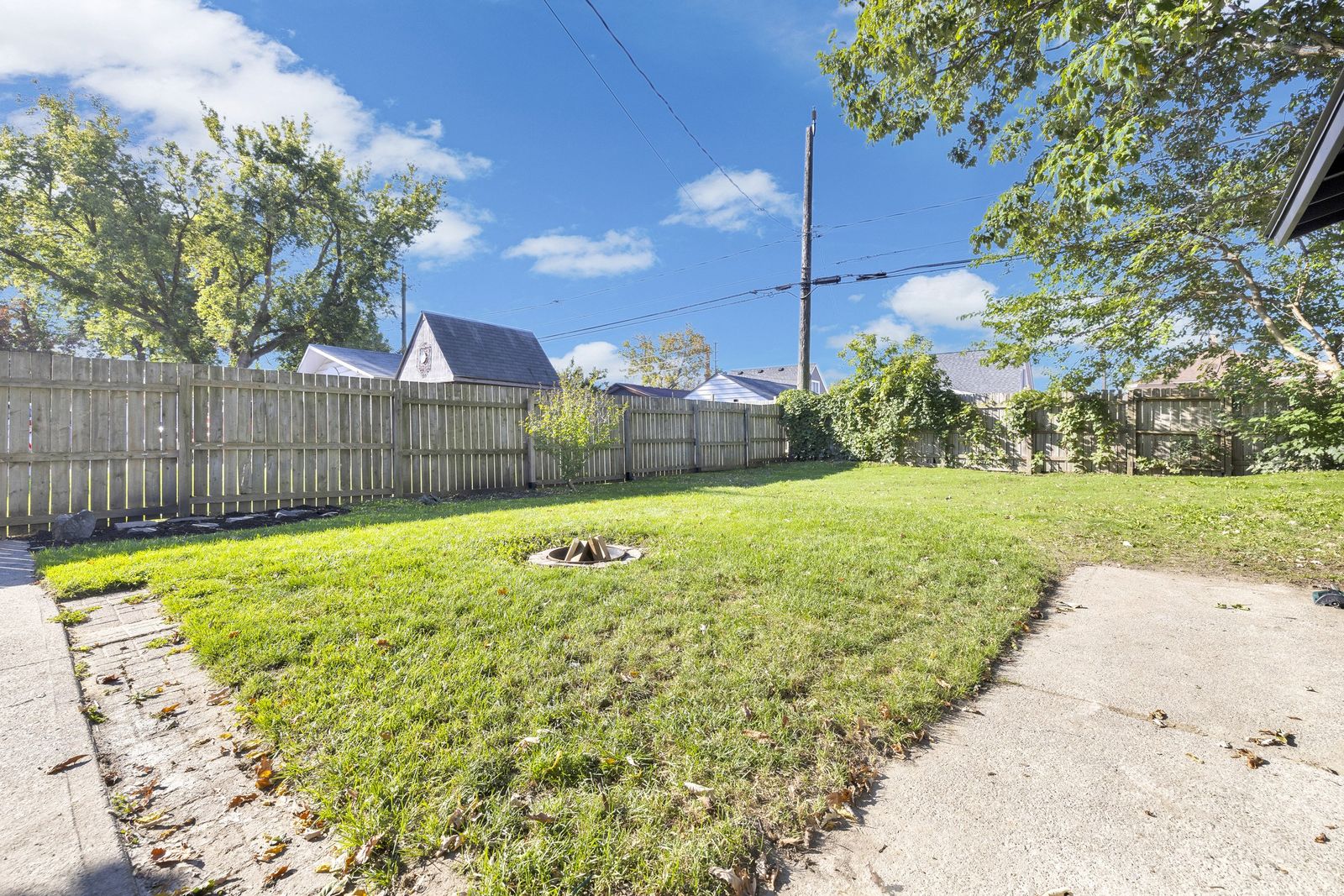 Backyard lawn with a fire pit, a wood fence and a concrete pad in the corner.