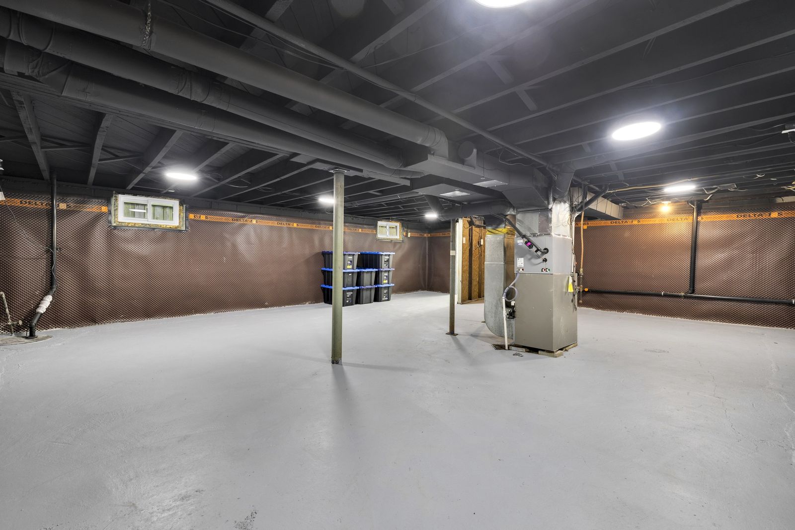 Unfinished basement with a painted concrete floor, black-painted ceiling, membrane on the walls and the furnace.