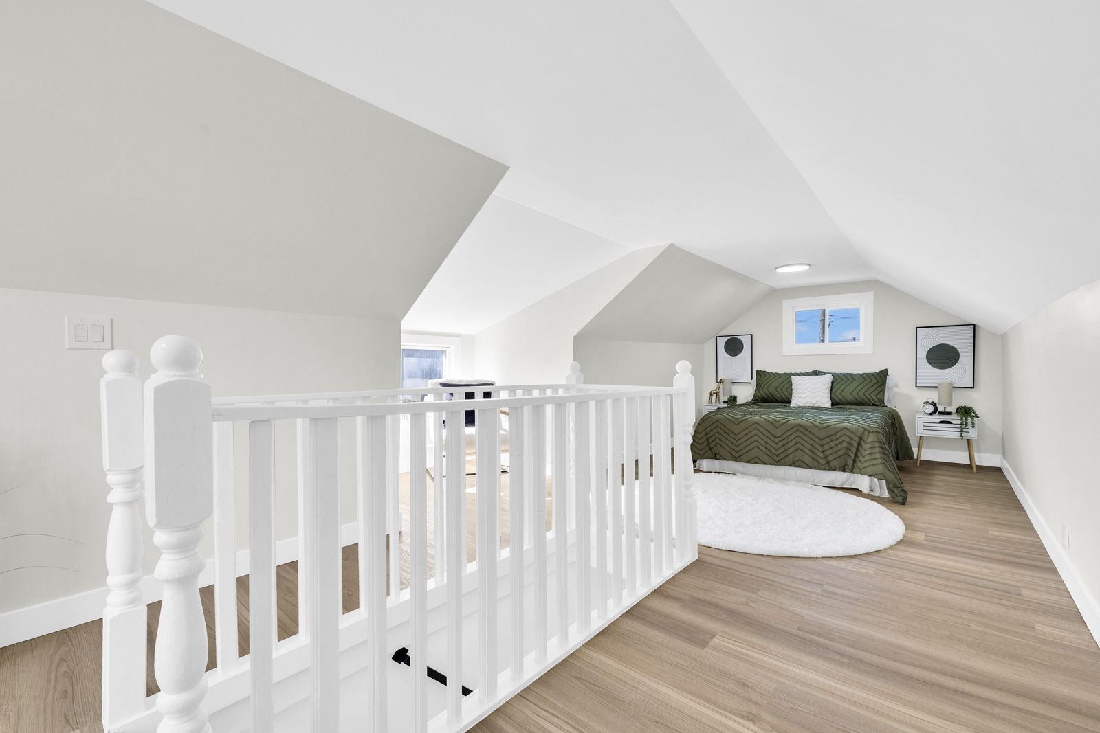 Upper level seen from the top of the stairs, with a white railing and the bed at the far end.