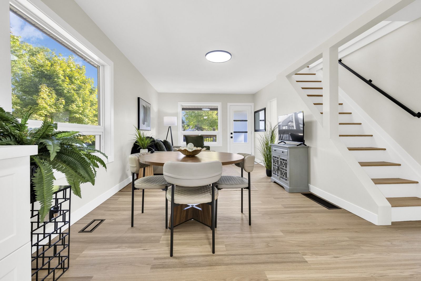 Dining area with a round table and four chairs, the stairs to the upper level and the back door beyond.
