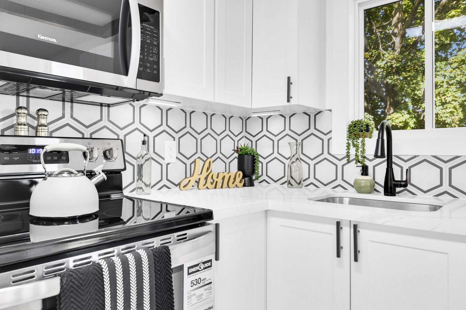 Kitchen corner with white cabinets, hexagon tile backsplash, a sink with a black faucet and a window.