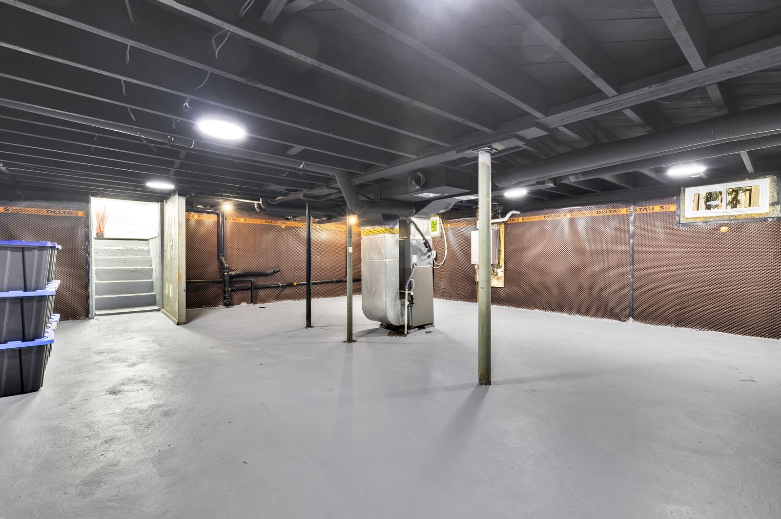 Unfinished basement with support posts, the furnace and the stairs up.