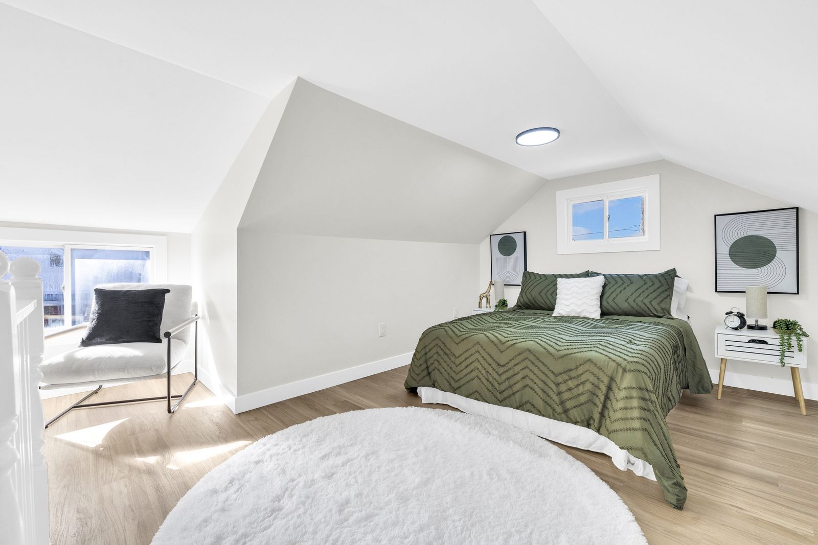 Upper-level bedroom with a bed, a round rug, a chair by the window and a sloped ceiling.