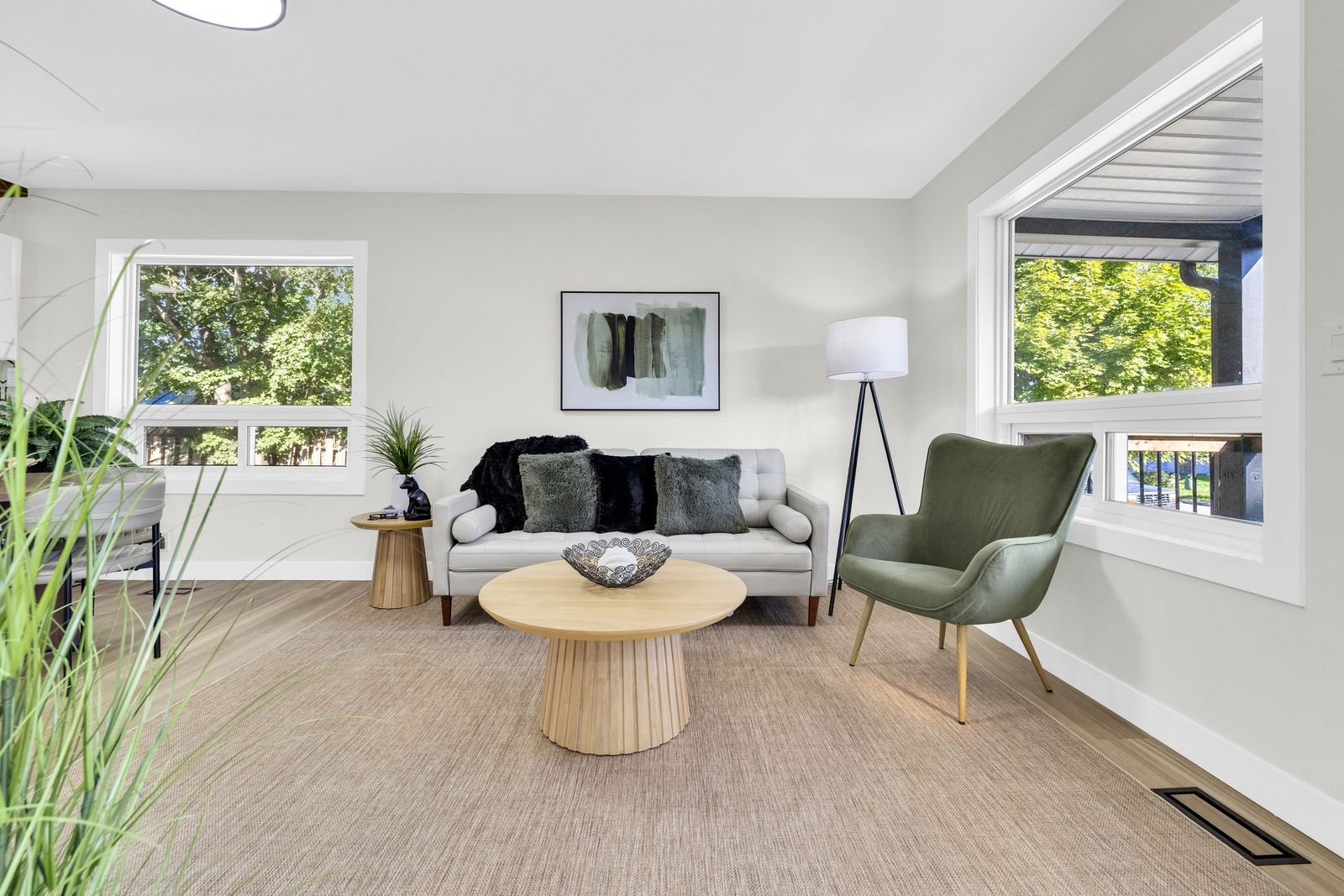 Living room with a sofa, a green armchair and a round coffee table, with windows on two walls.