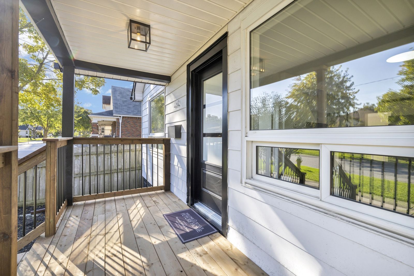 Covered front porch with wood decking and railing, a black front door and the front window.