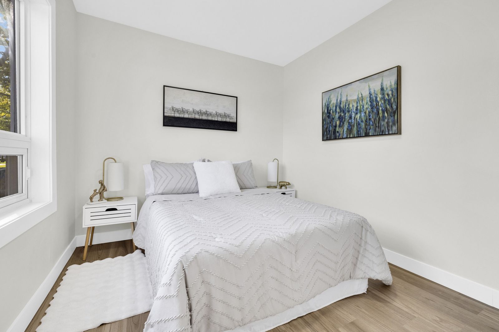 Bedroom with a bed, a white nightstand and two framed pictures.
