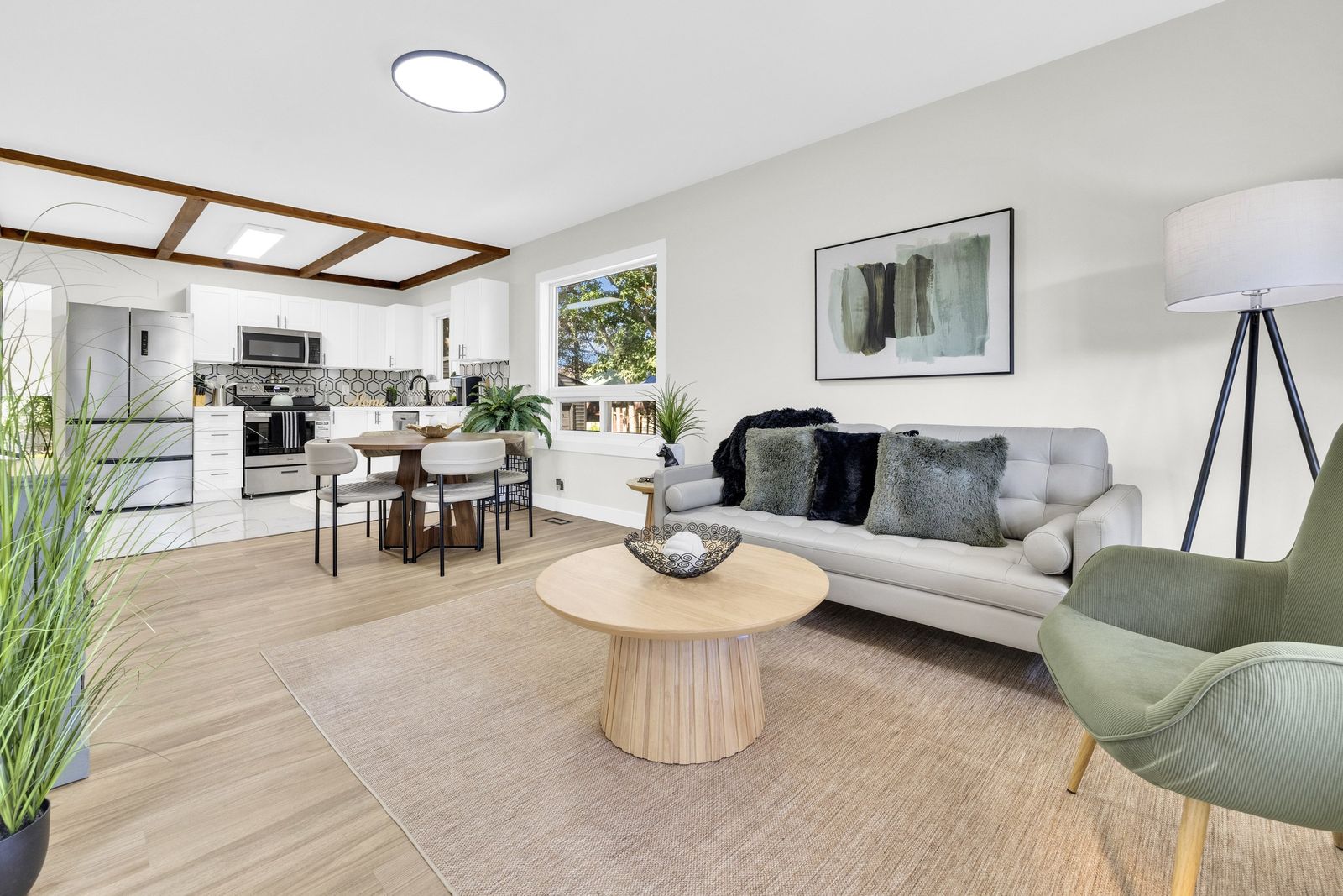 Living room with a sofa and green armchair, open to the dining area and kitchen under wood ceiling beams.