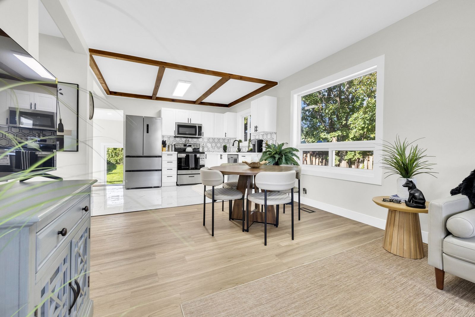 Dining table and kitchen seen from the living room, with wood ceiling beams and a large side window.