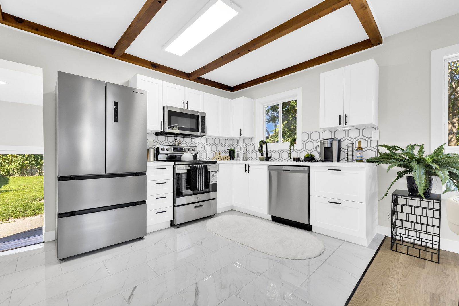 Kitchen with white cabinets, stainless steel refrigerator, stove, microwave and dishwasher, a hexagon tile backsplash and wood ceiling beams.