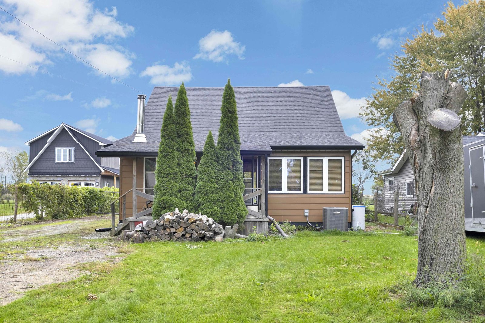 One-and-a-half-storey house with brown siding, a covered front porch, evergreens and a front lawn.