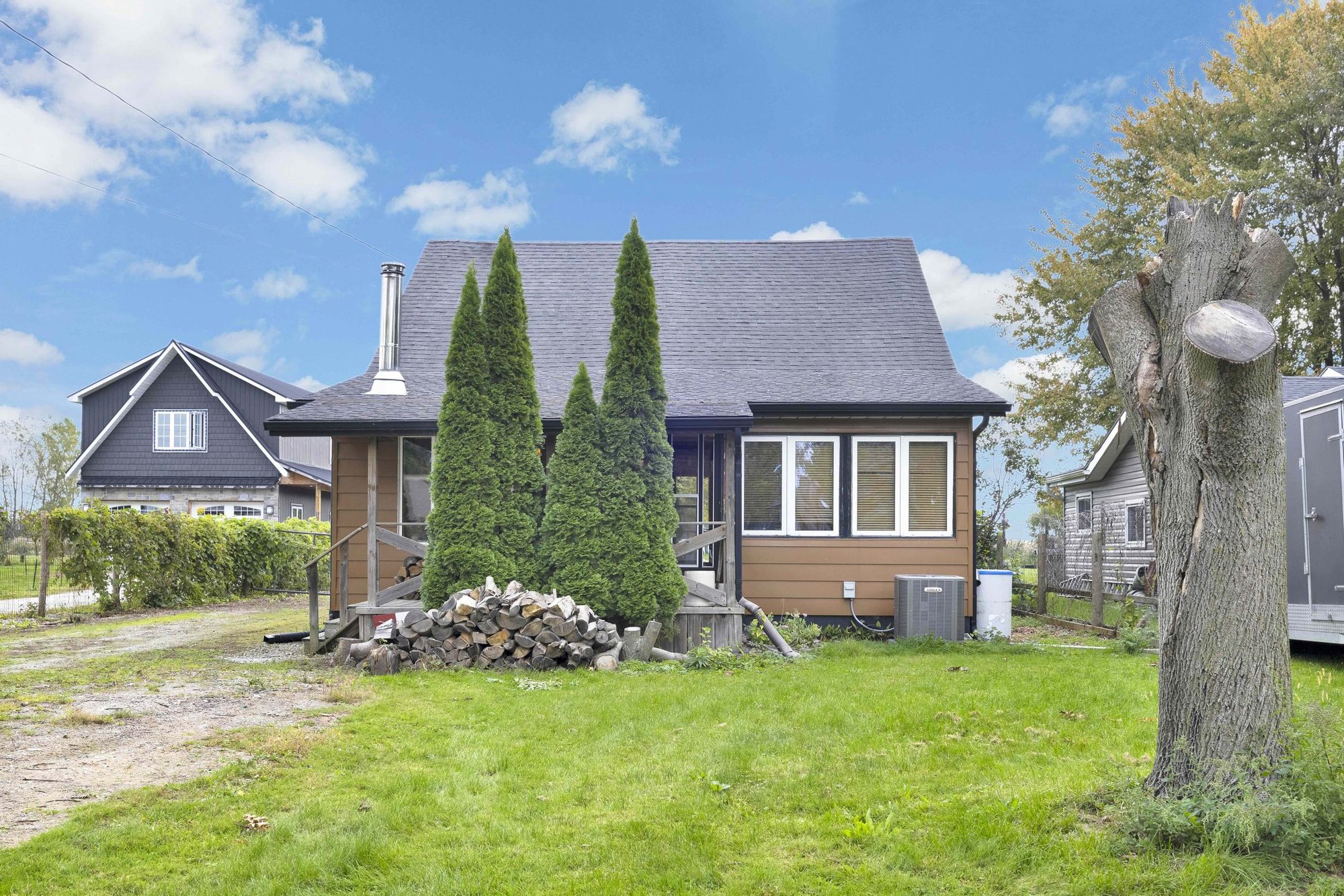 One-and-a-half-storey house with brown siding, a covered front porch, evergreens and a front lawn.