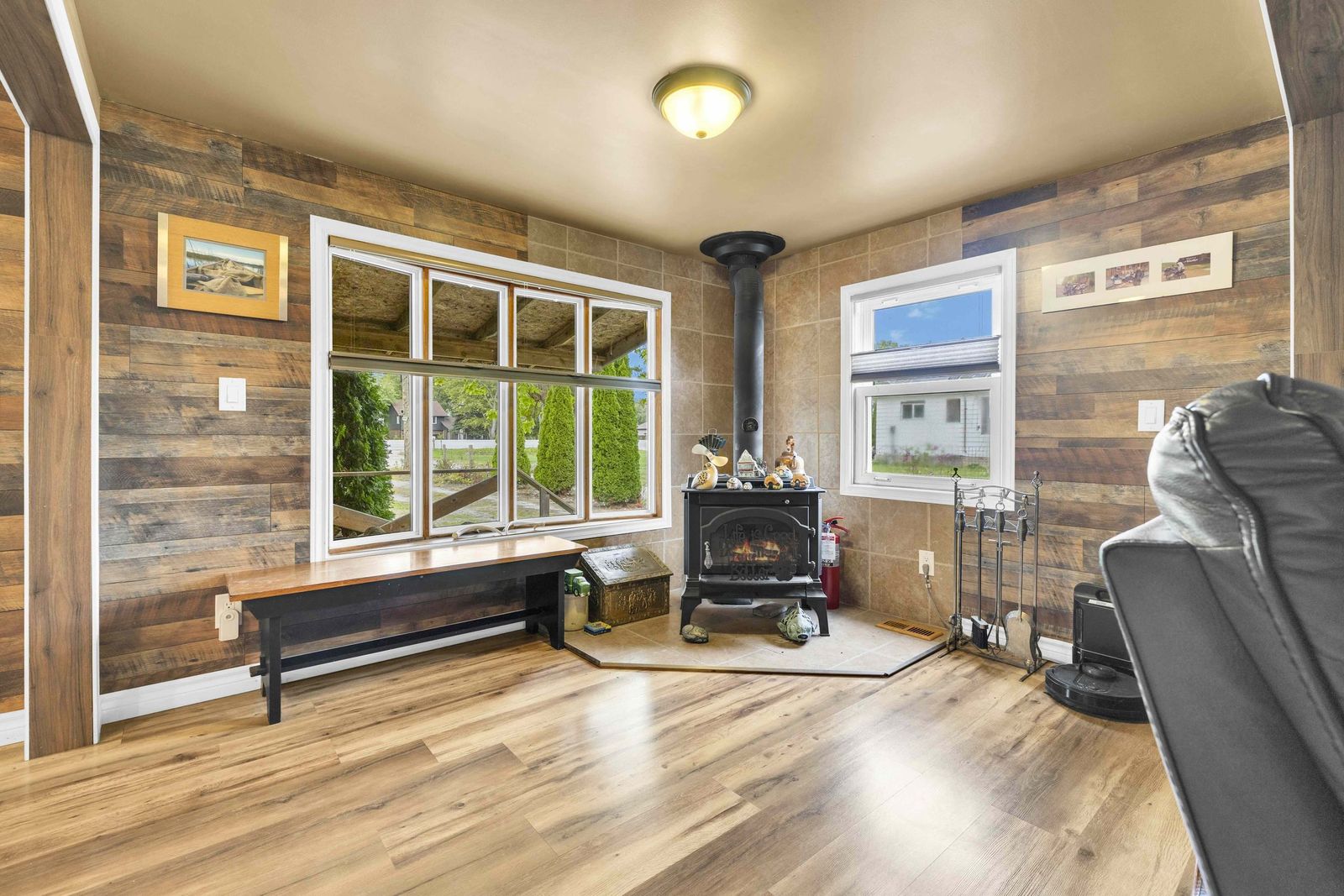 Room with a wood-burning stove, wood-plank walls and a large window.