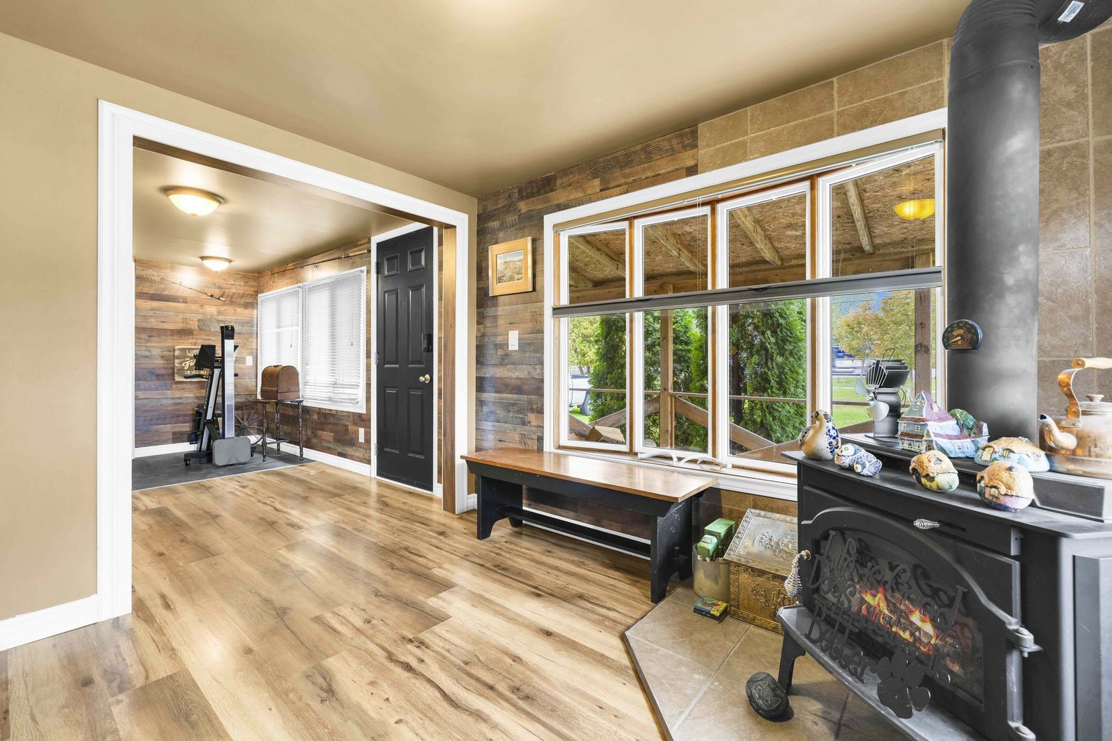 Living room with a wood-burning stove, wood-plank wall and a large window.