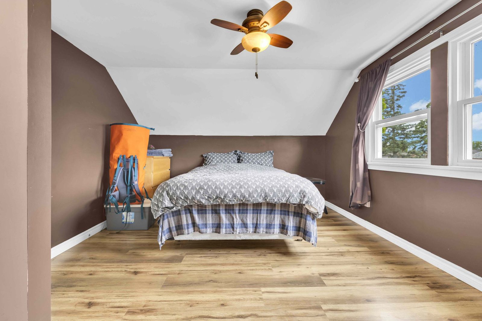 Bedroom with a bed, dresser, two curtained windows and a ceiling fan.