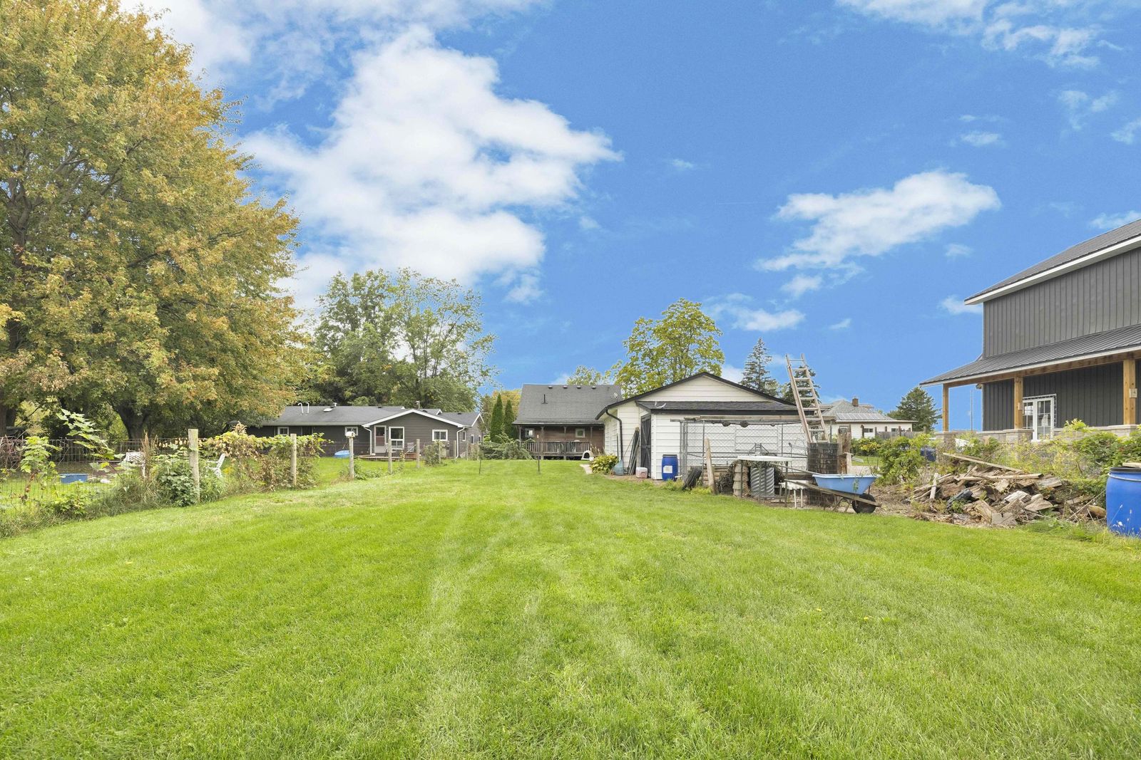 Long backyard lawn with fencing, outbuildings and trees.