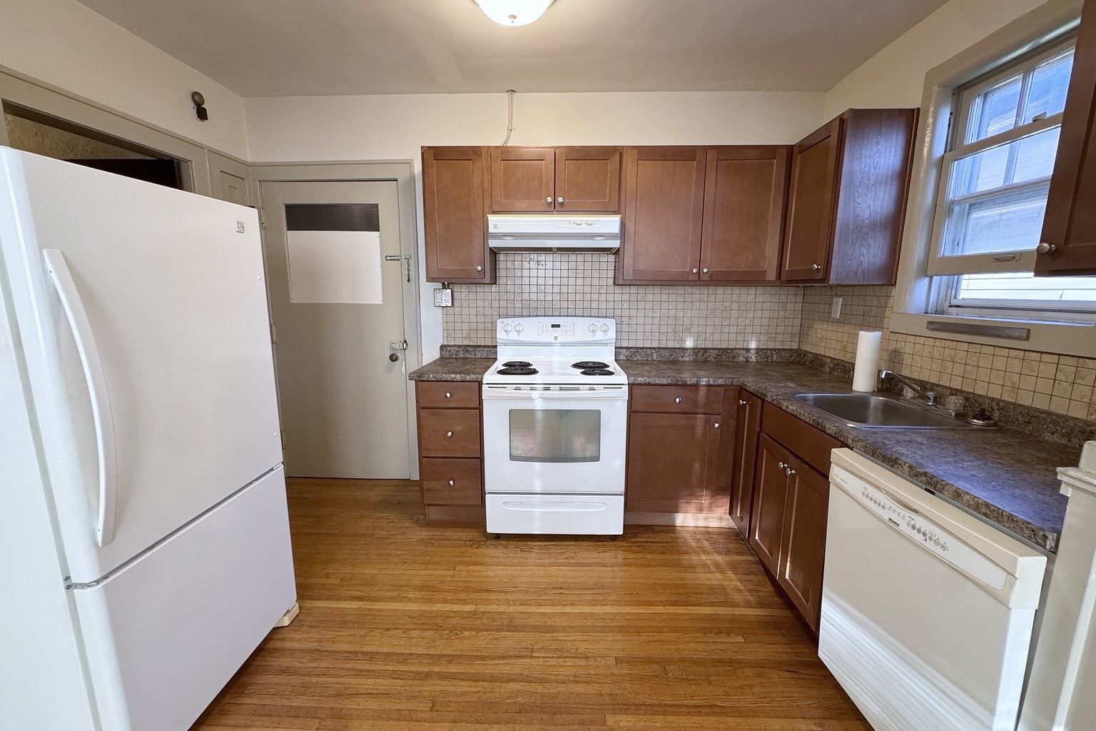 Kitchen with wood cabinets, a white refrigerator, stove and dishwasher, and a sink under the window.