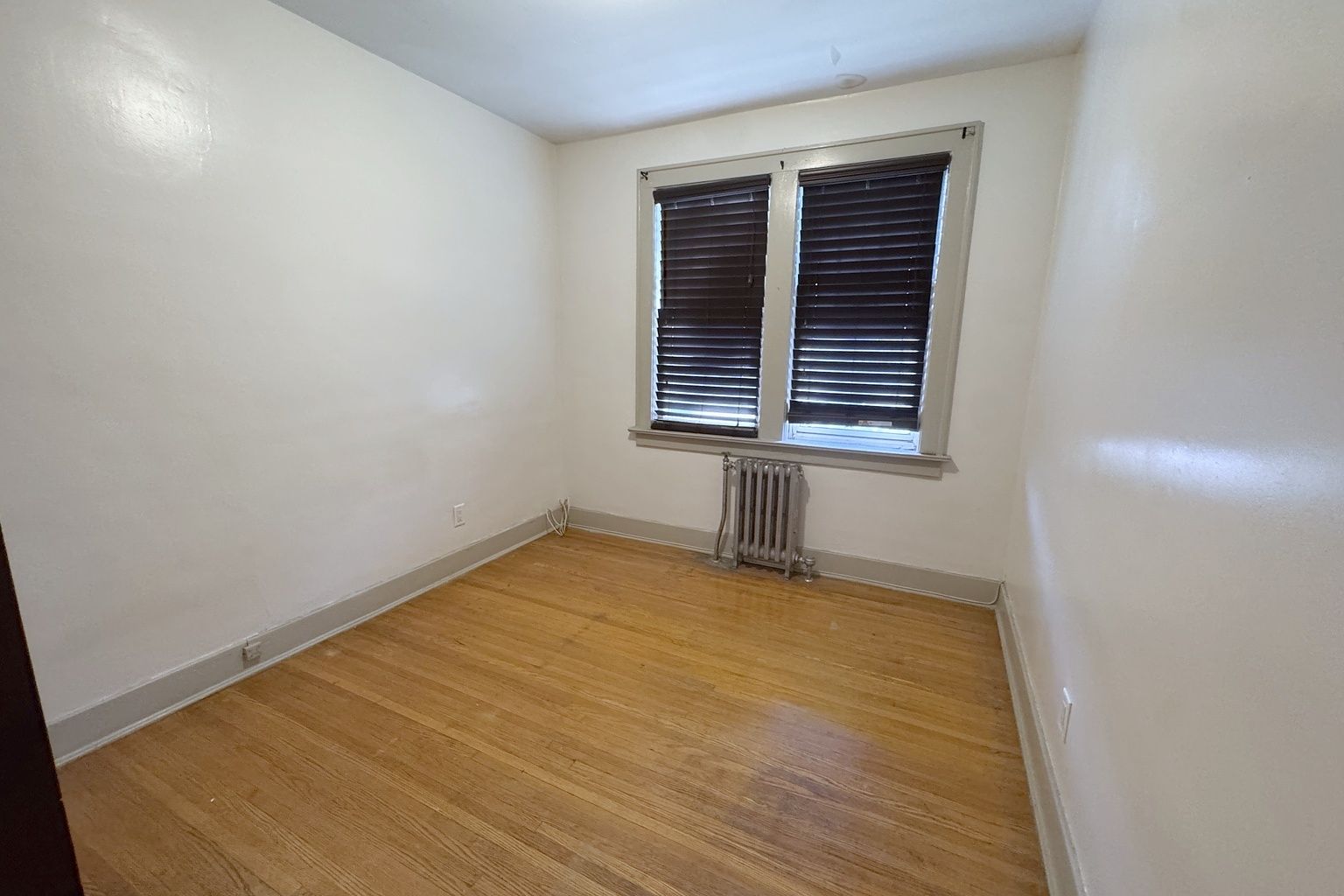 Empty bedroom with a wood floor, a double window and a radiator beneath it.