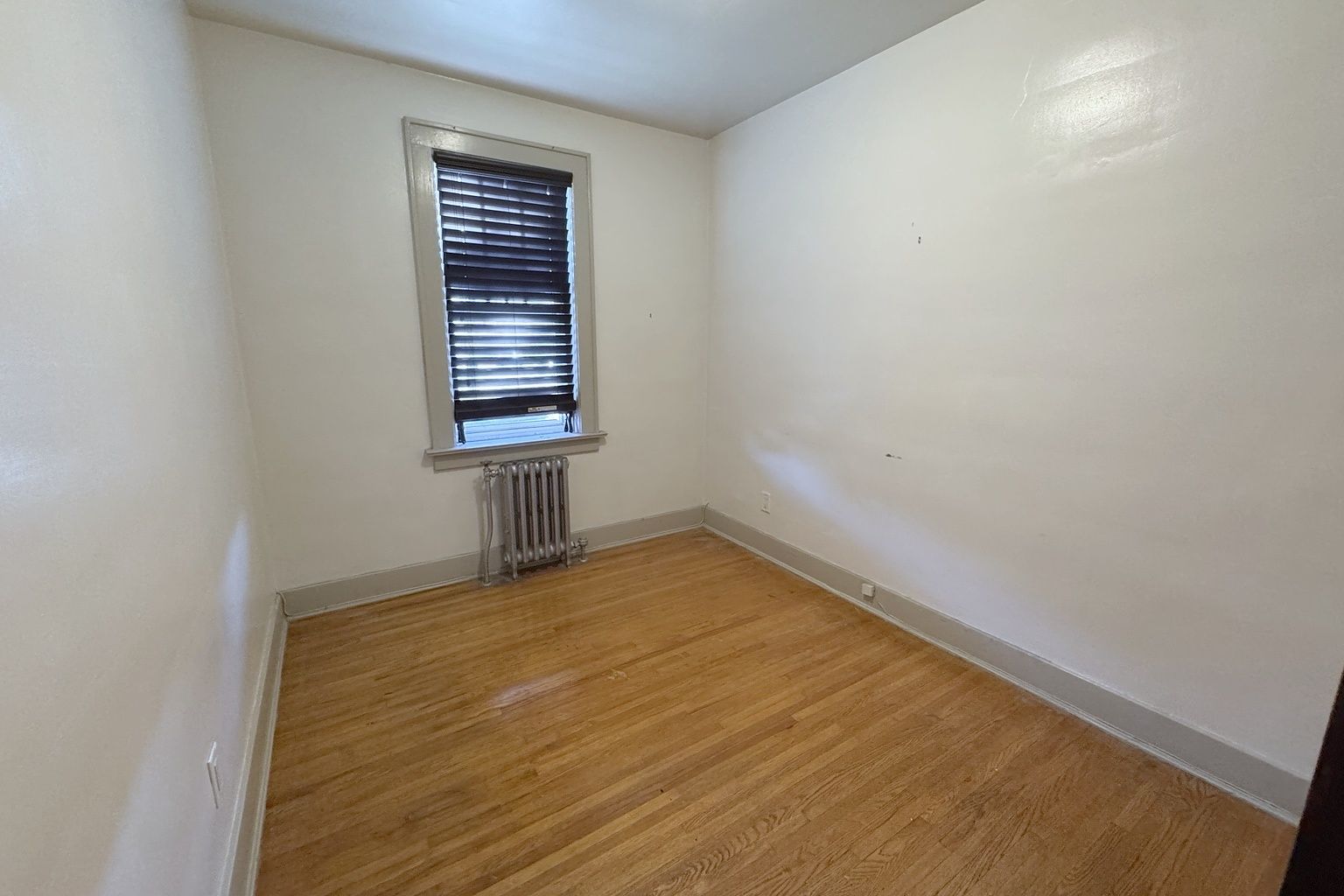 Empty bedroom with a wood floor, a single window and a radiator beneath it.