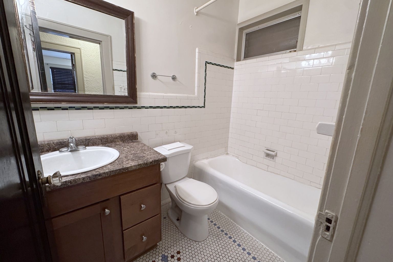 Bathroom with a bathtub, toilet, vanity and mirror, white wall tile and a hexagonal tile floor.