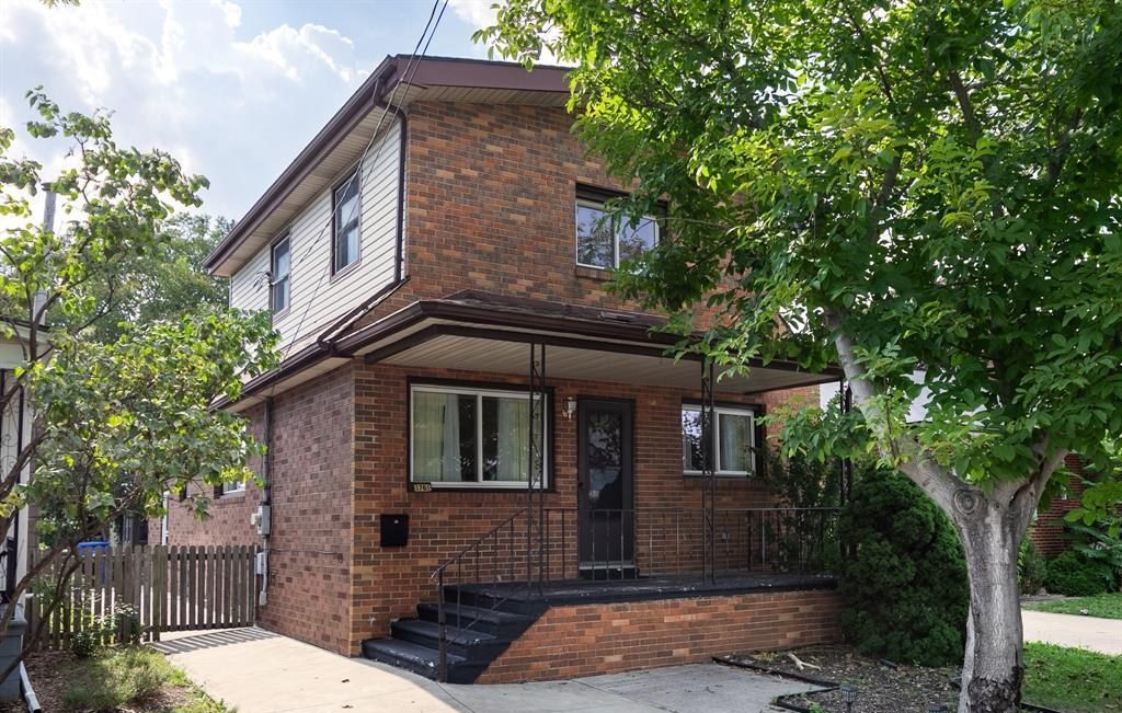 Two-storey brick house with a covered entry and a tree in the front yard.