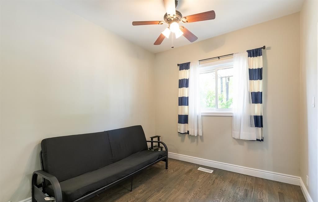 Room with a ceiling fan, a futon and a curtained window.