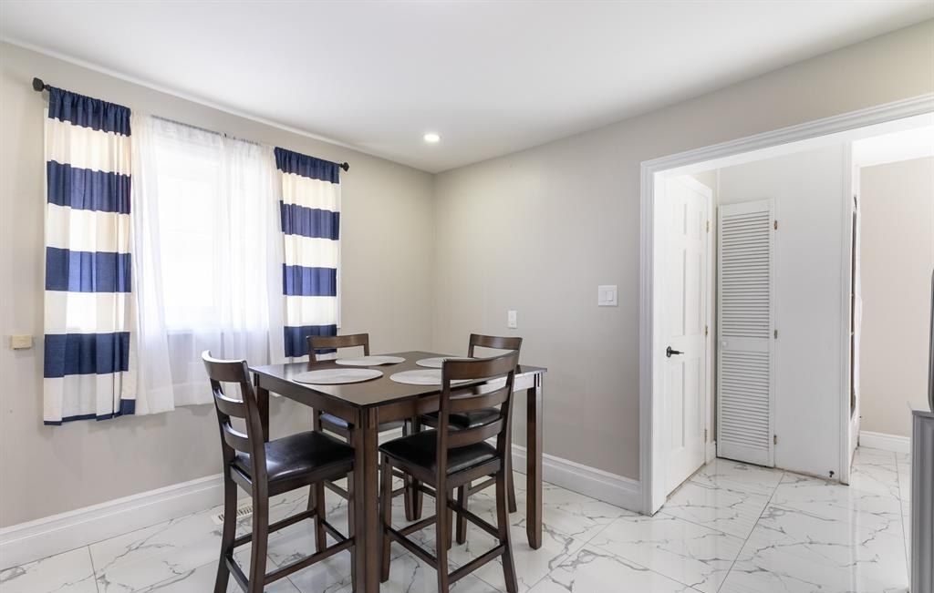 Dining table with four chairs beside a curtained window.