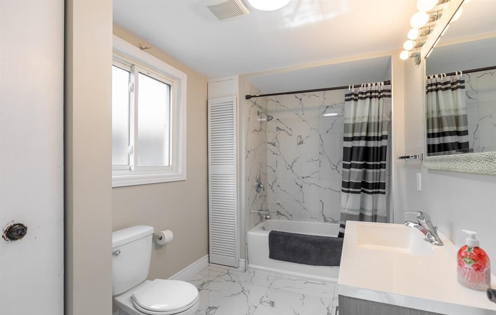 Bathroom with a bathtub and shower, a toilet, a vanity and a window.