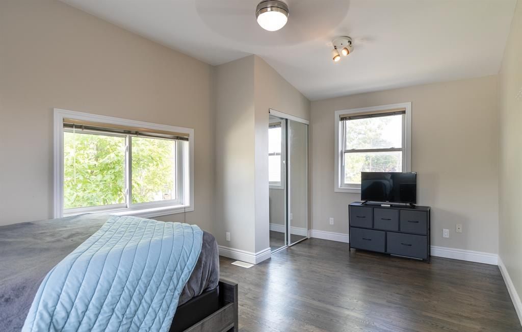 Bedroom with a bed, two windows and a mirrored closet.