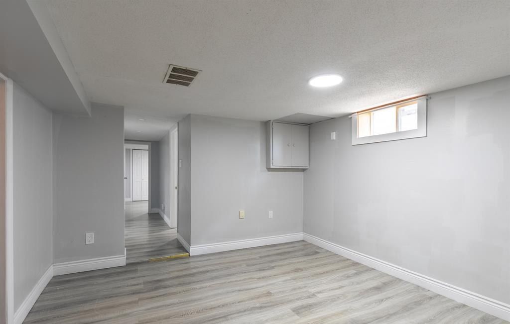 Empty room with grey walls, a small high window and plank flooring.