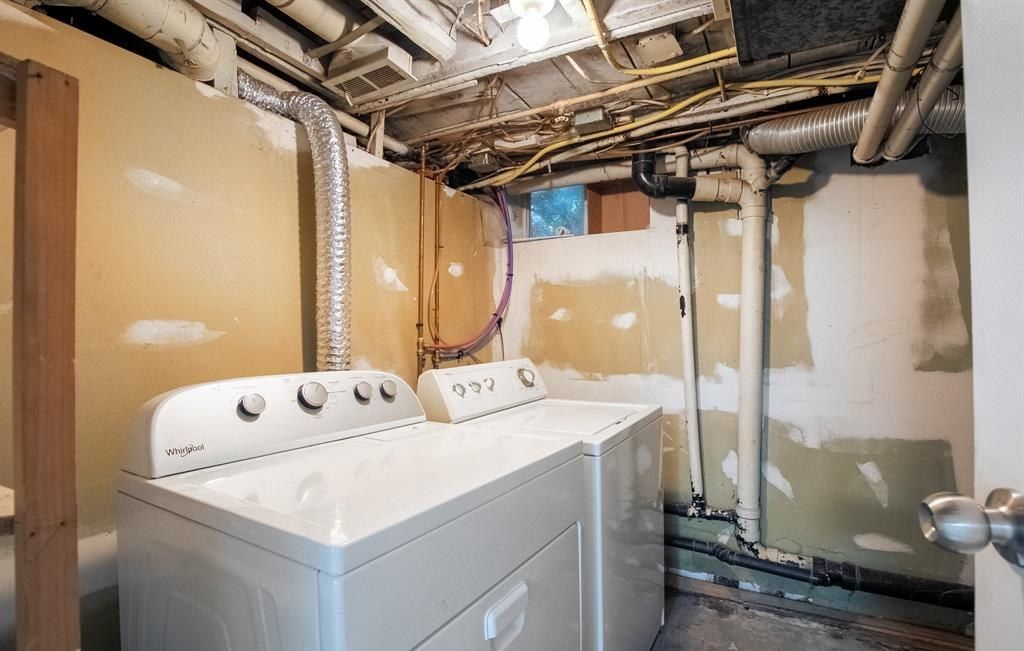 Washer and dryer in a utility room with exposed joists and pipes.